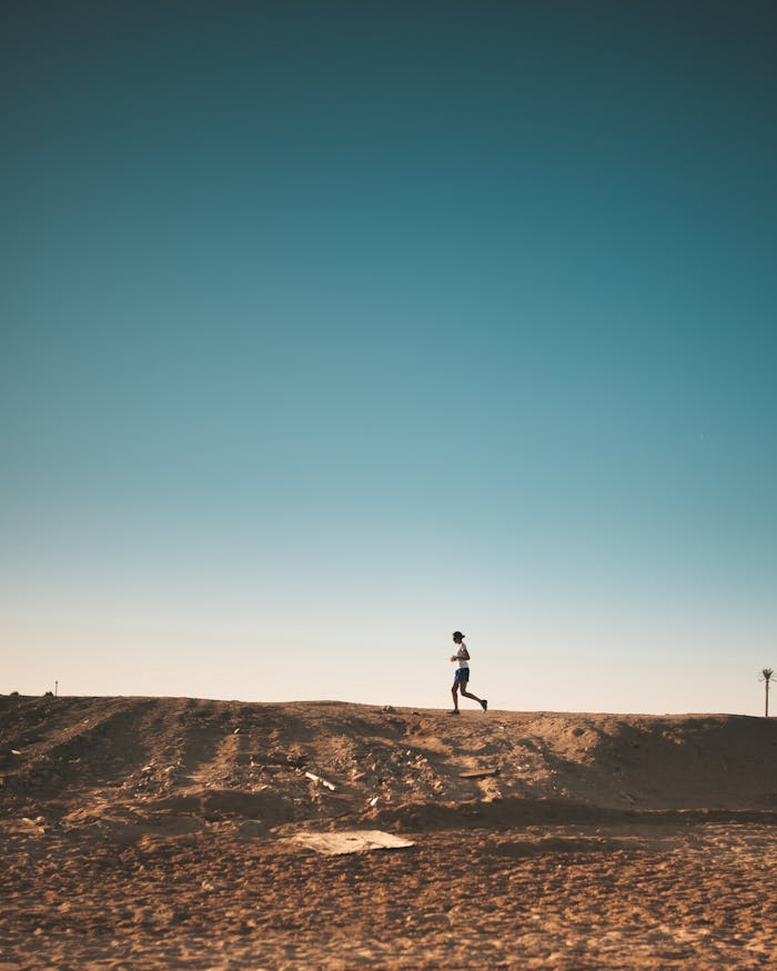 Home A person jogs on a sandy path with a vast blue sky above, capturing movement and freedom.